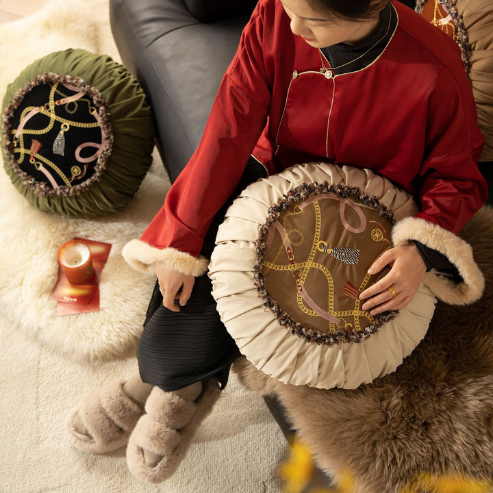 Round decorative pillow with pleated edge, fringe trim, and chain tassel motif