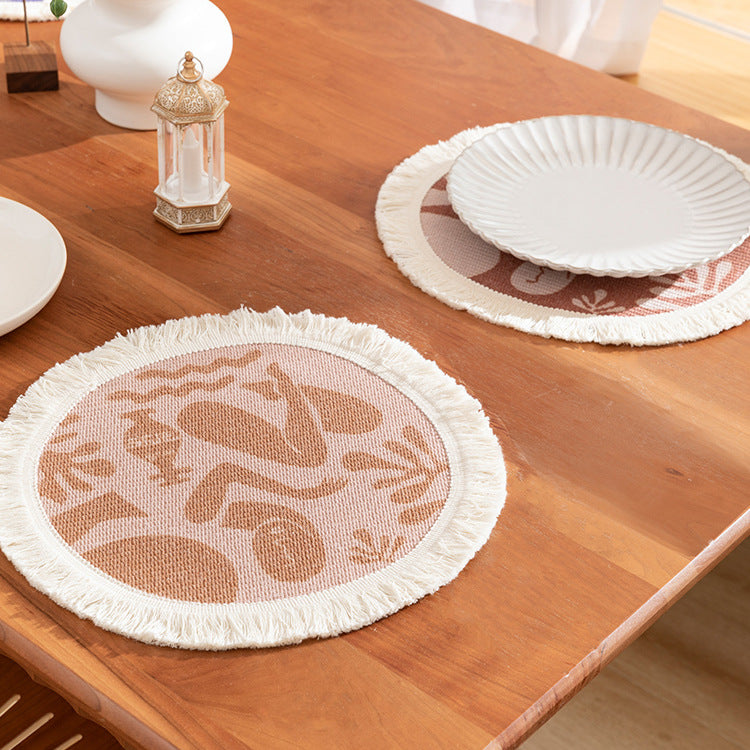 Round woven placemat with fringes and abstract figure motif