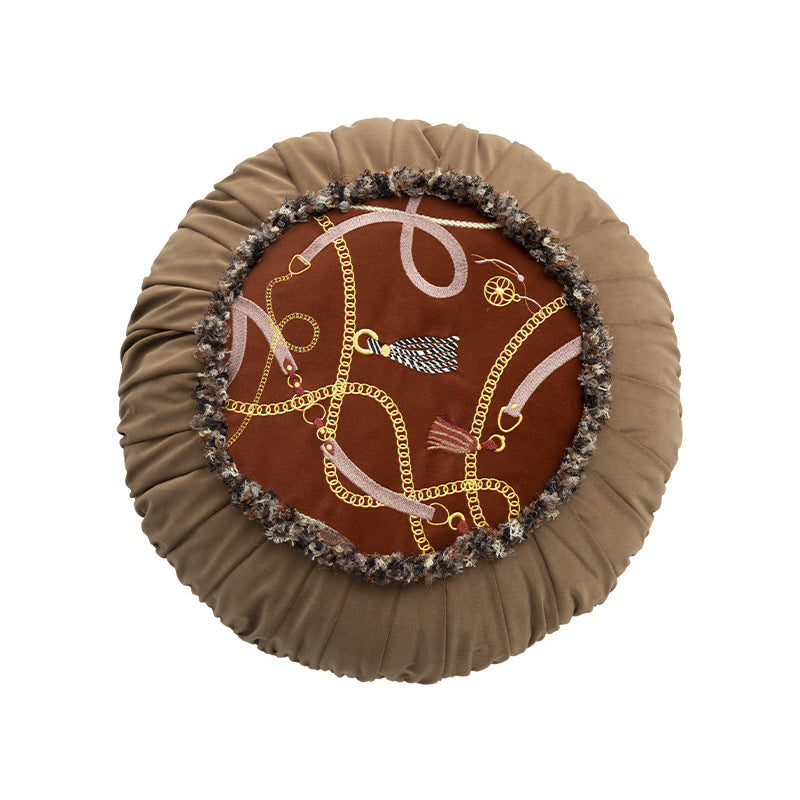 Round decorative pillow with pleated edge, fringe trim, and chain tassel motif