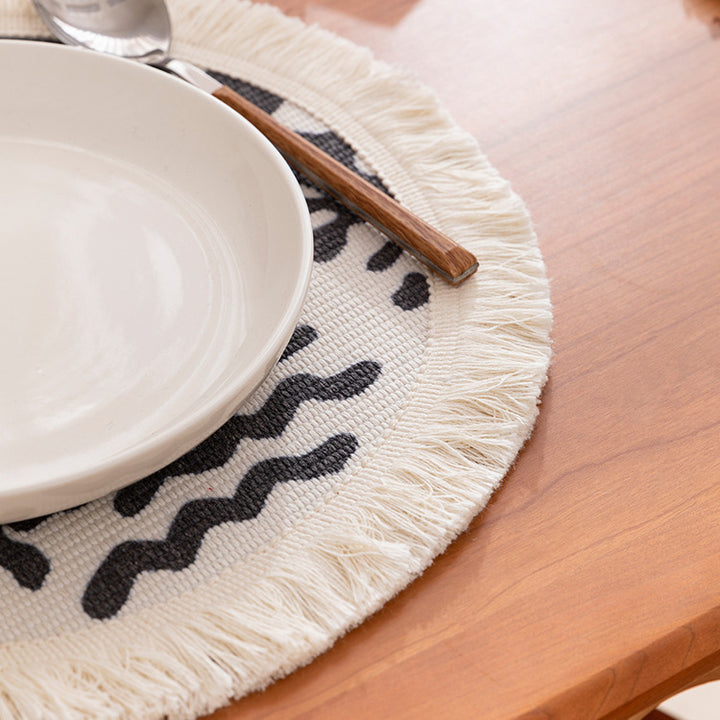 Round woven placemat with fringes and abstract figure motif